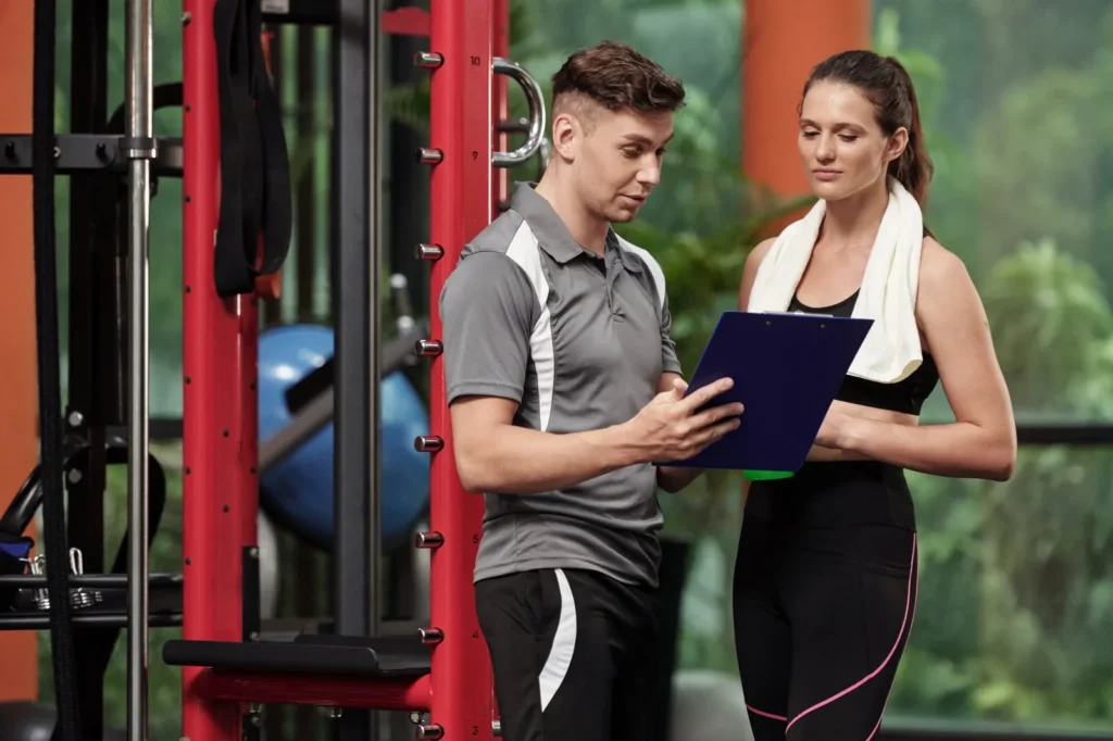Personal trainer reviewing a fitness plan with a client at the gym, explaining options and answering how much does a personal trainer cost.